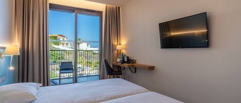 Quarto de hotel com cama, escrivaninha, cadeira, televisão e varanda com vista para edifícios.