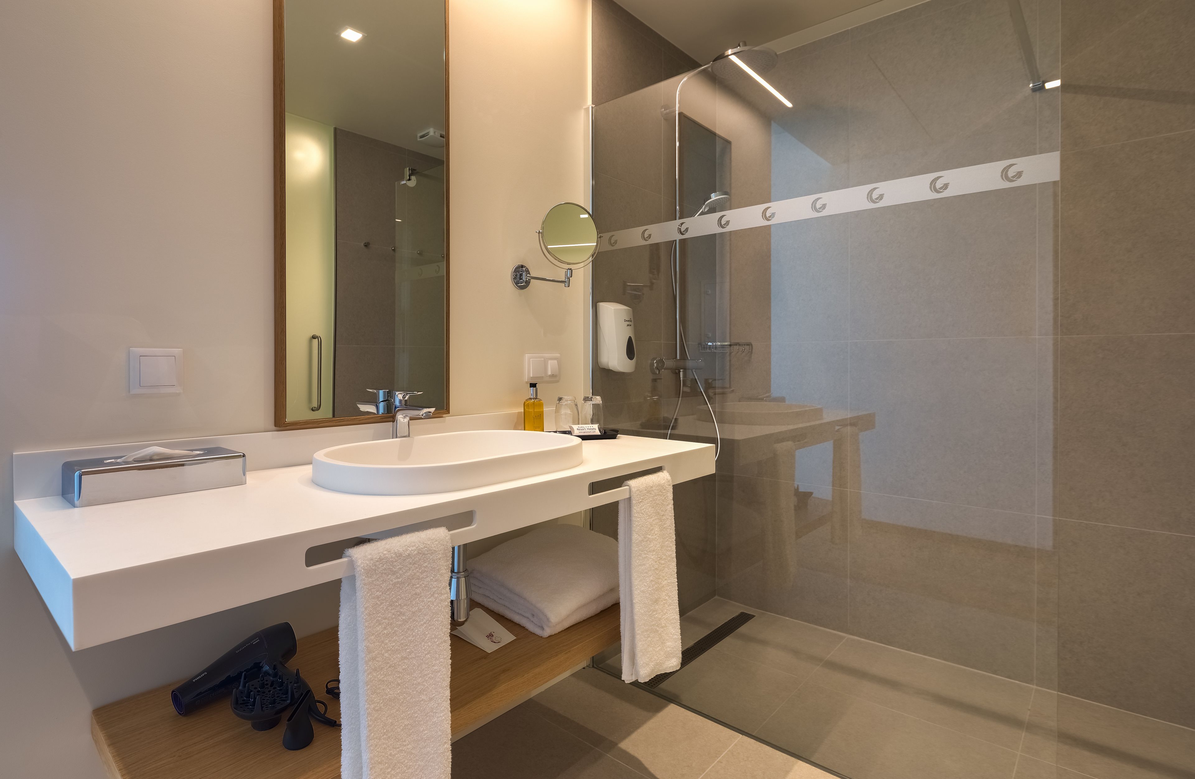 A modern bathroom with a white sink, mirror, and glass shower enclosure.