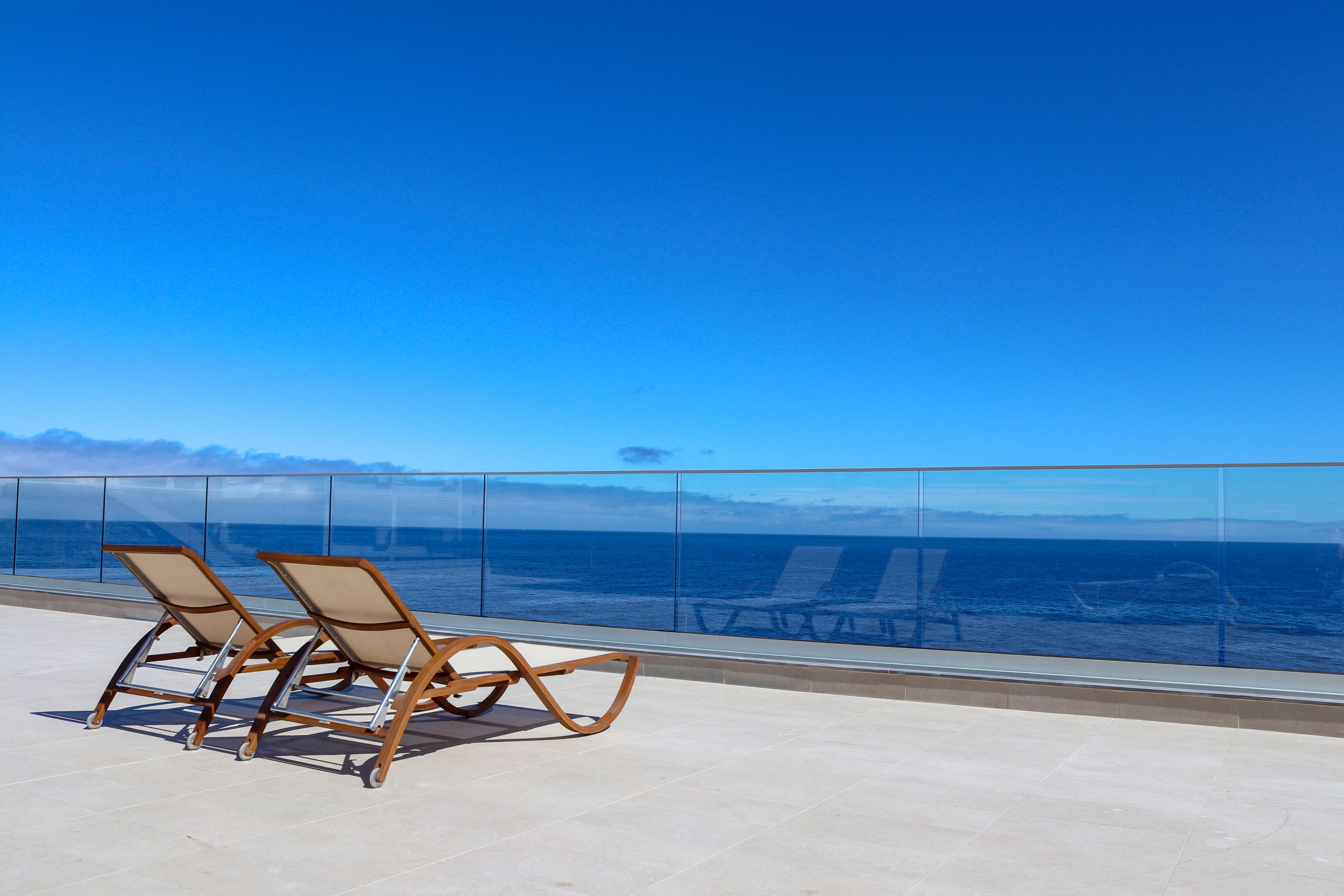 Un balcon avec deux fauteuils confortables donnant sur un ciel bleu dégagé et offrant une vue sur l’océan.