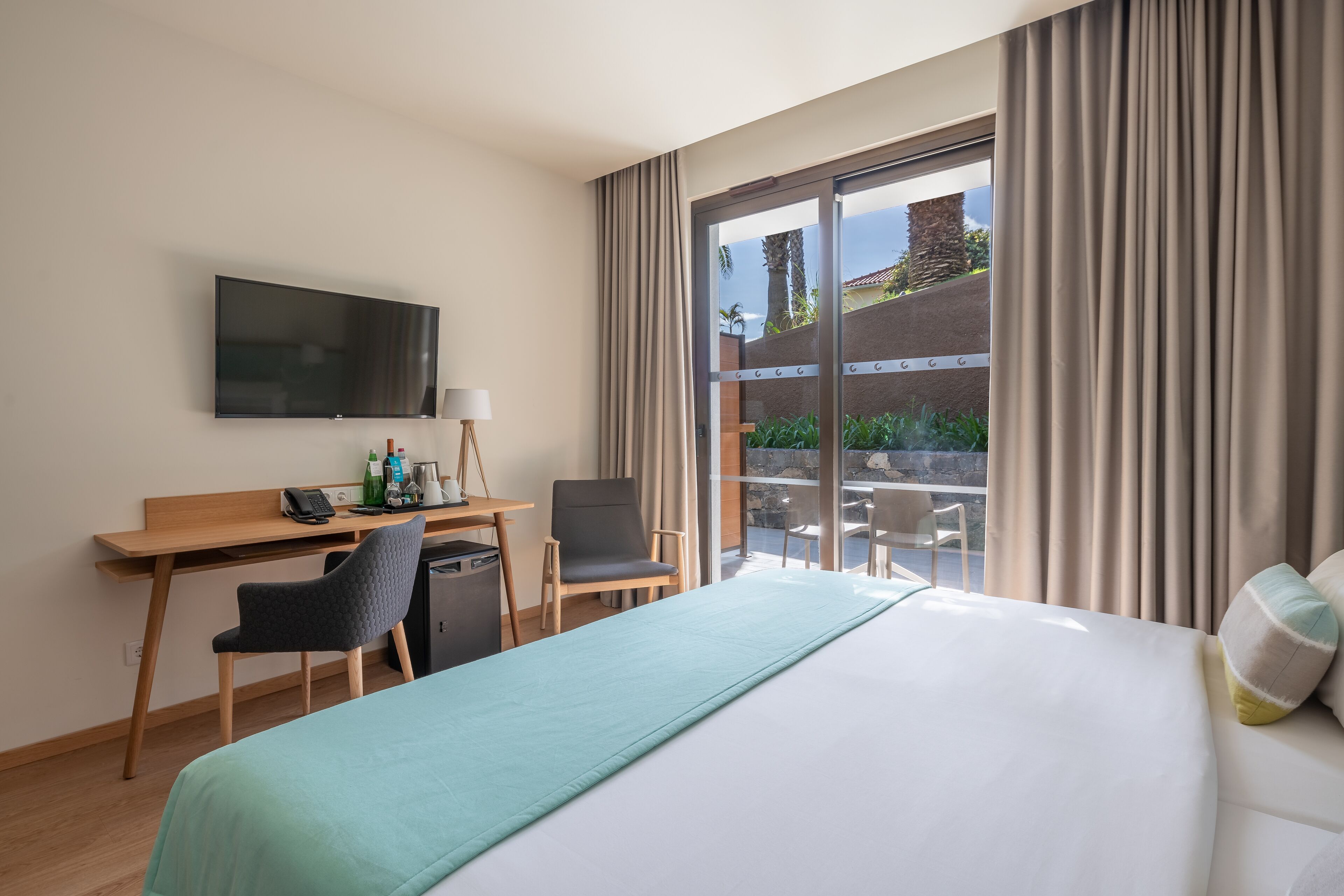 A hotel room with a bed, a desk with a computer, a chair, a TV, and a view of the outdoors.