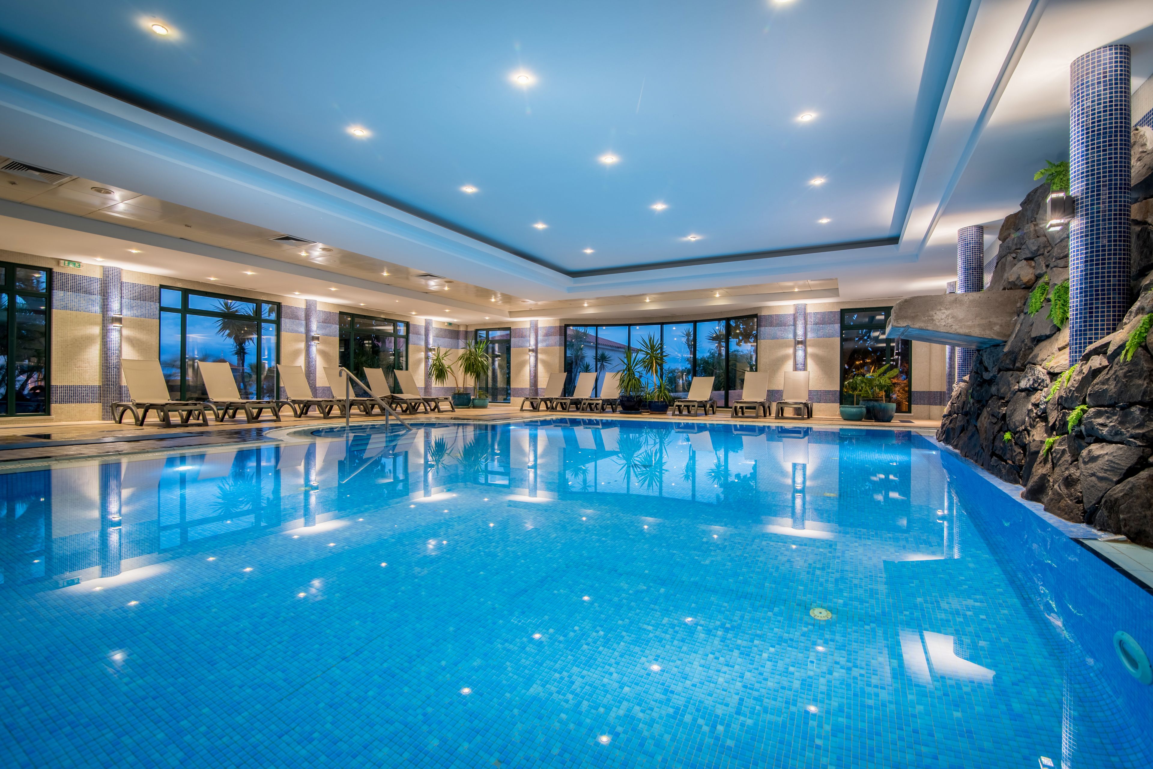 Una piscina techada, una piscina al aire libre, sombrillas