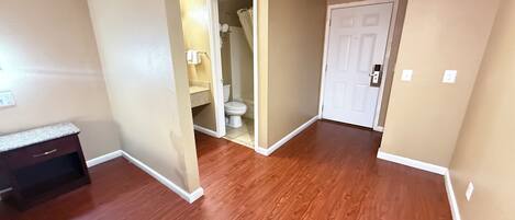 A hallway with wooden flooring, a white door, and a bathroom visible through an open door.