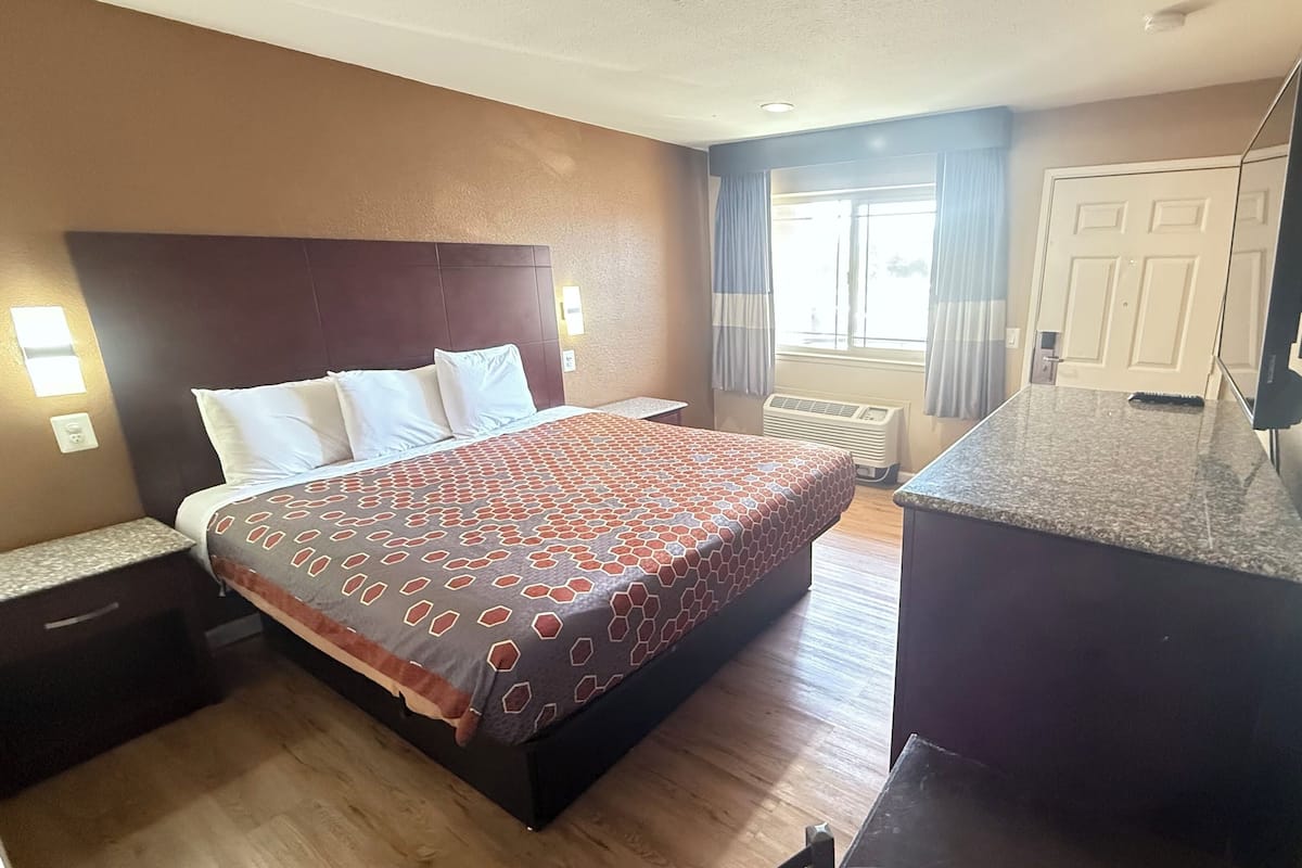 A hotel room with a bed, bedside tables, a desk, a TV, and a window with curtains.