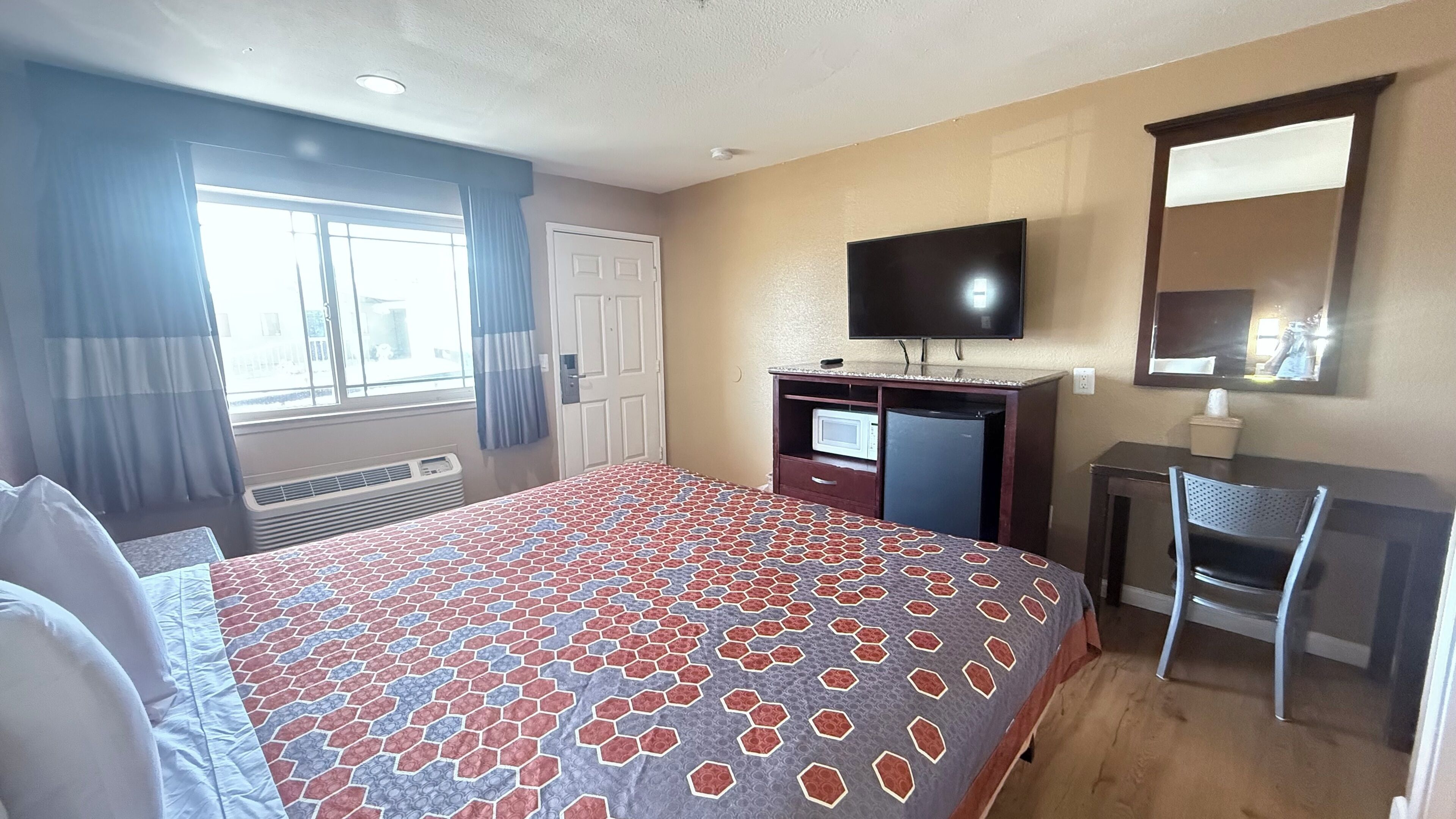 Een hotelkamer met een groot bed, een bureau met een computer, een televisie en een raam met gordijnen.
