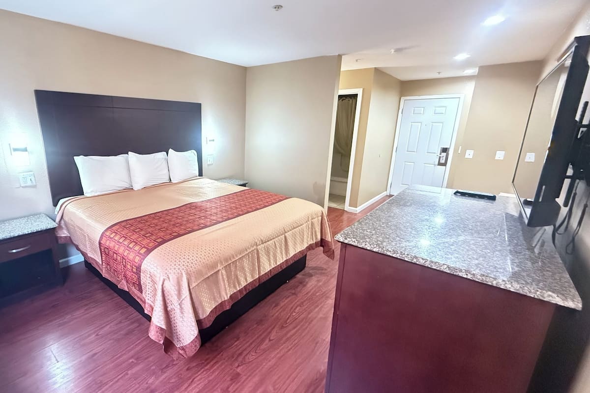 A hotel room with a bed, a nightstand, a desk, and a kitchenette.