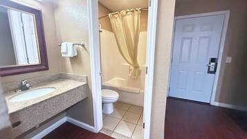 A bathroom with a granite countertop sink, a toilet, and a shower with a beige curtain.