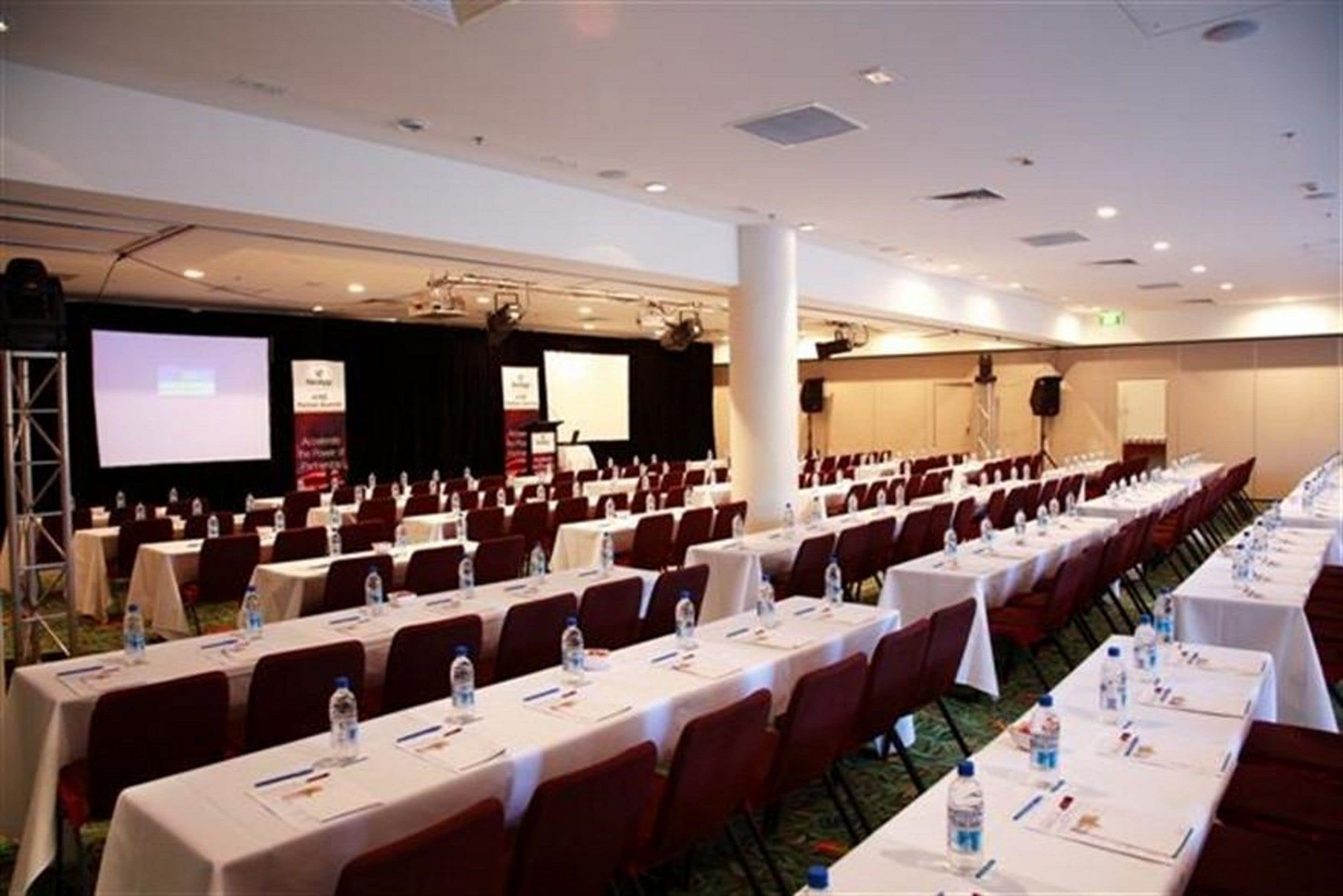 A conference room with rows of tables, chairs, and a stage with a screen.