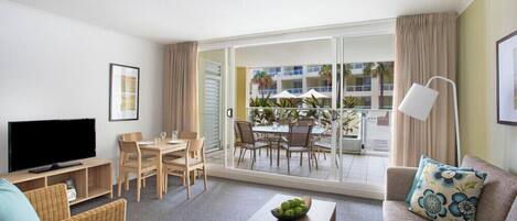Ein modernes Wohnzimmer mit Flachbildfernseher, einer Couch, einem Couchtisch und einem Essbereich mit Tisch und Stühlen.