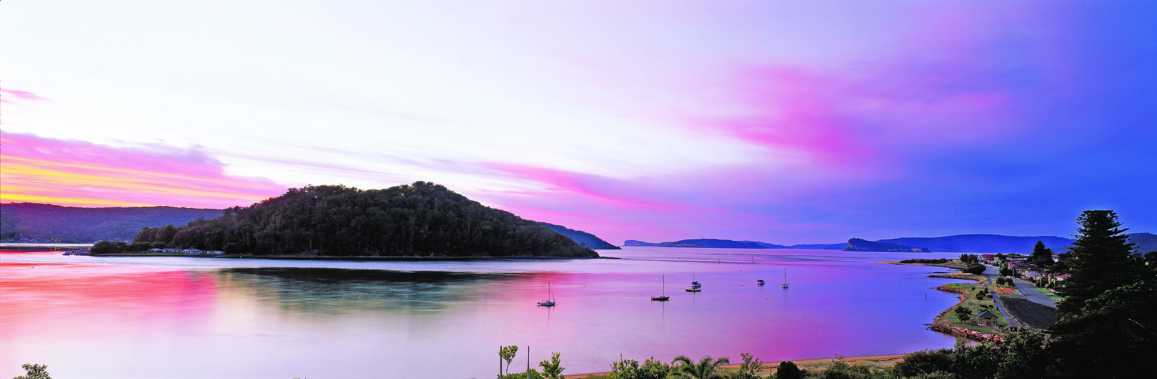 Eine friedliche Uferlandschaft mit einer kleinen Insel, ruhigem Wasser und fernen Bergen.