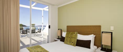 A hotel room with a large bed, a nightstand, a lamp, and a view of the outdoors.
