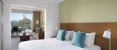 Habitación de hotel con una cama grande, una mesita de noche con lámpara, una pequeña mesa con un frutero y vistas al exterior.