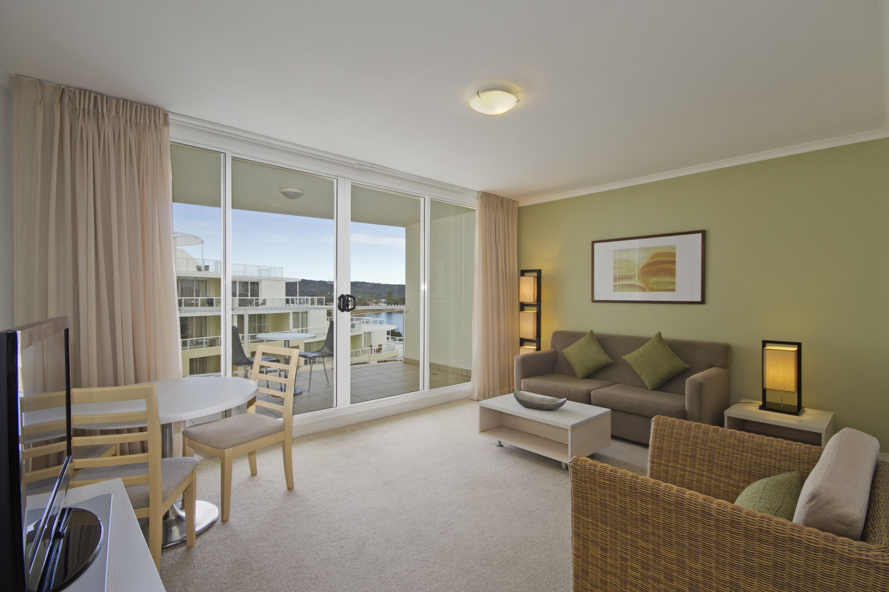 A living room with a balcony, a television, a dining table with chairs, a sofa, and a framed picture on the wall.