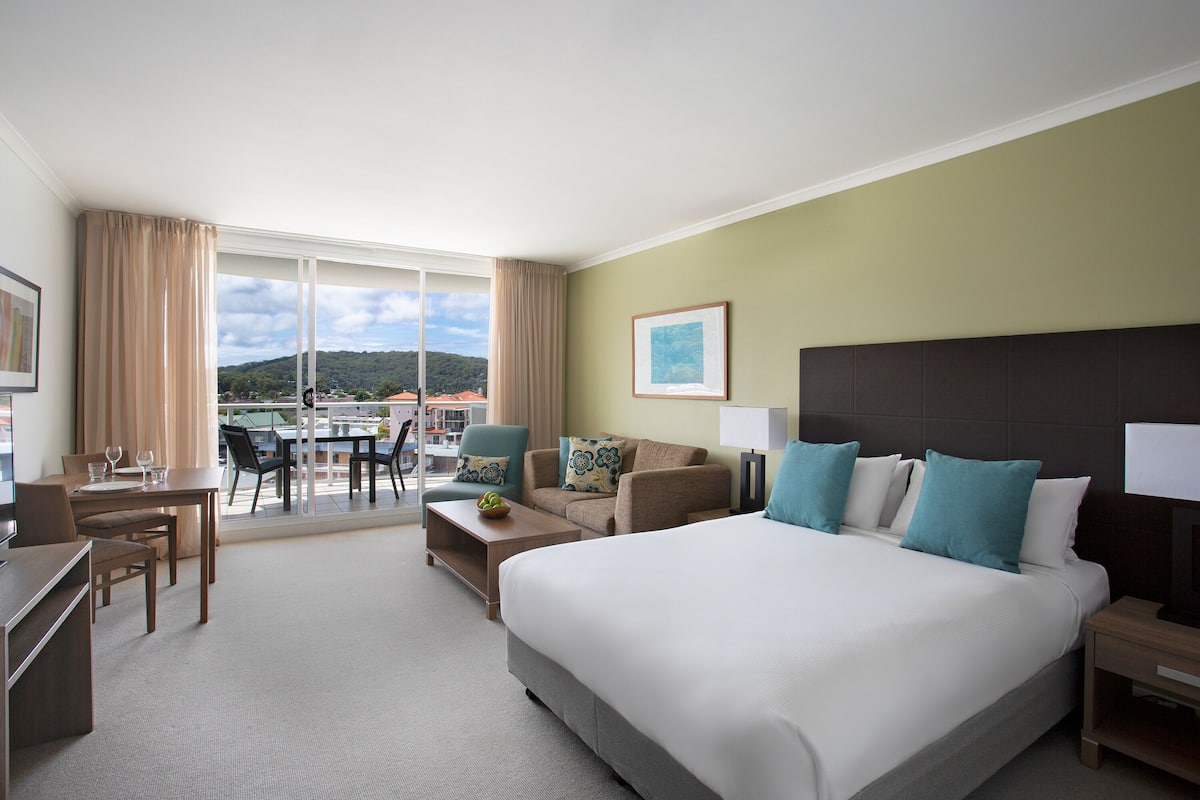 Une chambre d’hôtel avec un grand lit, un bureau, une chaise, un canapé et un balcon offrant une vue sur la ville.