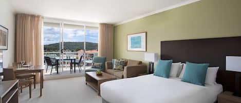A hotel room with a large bed, a desk, a chair, a sofa, and a balcony with a view of the city.