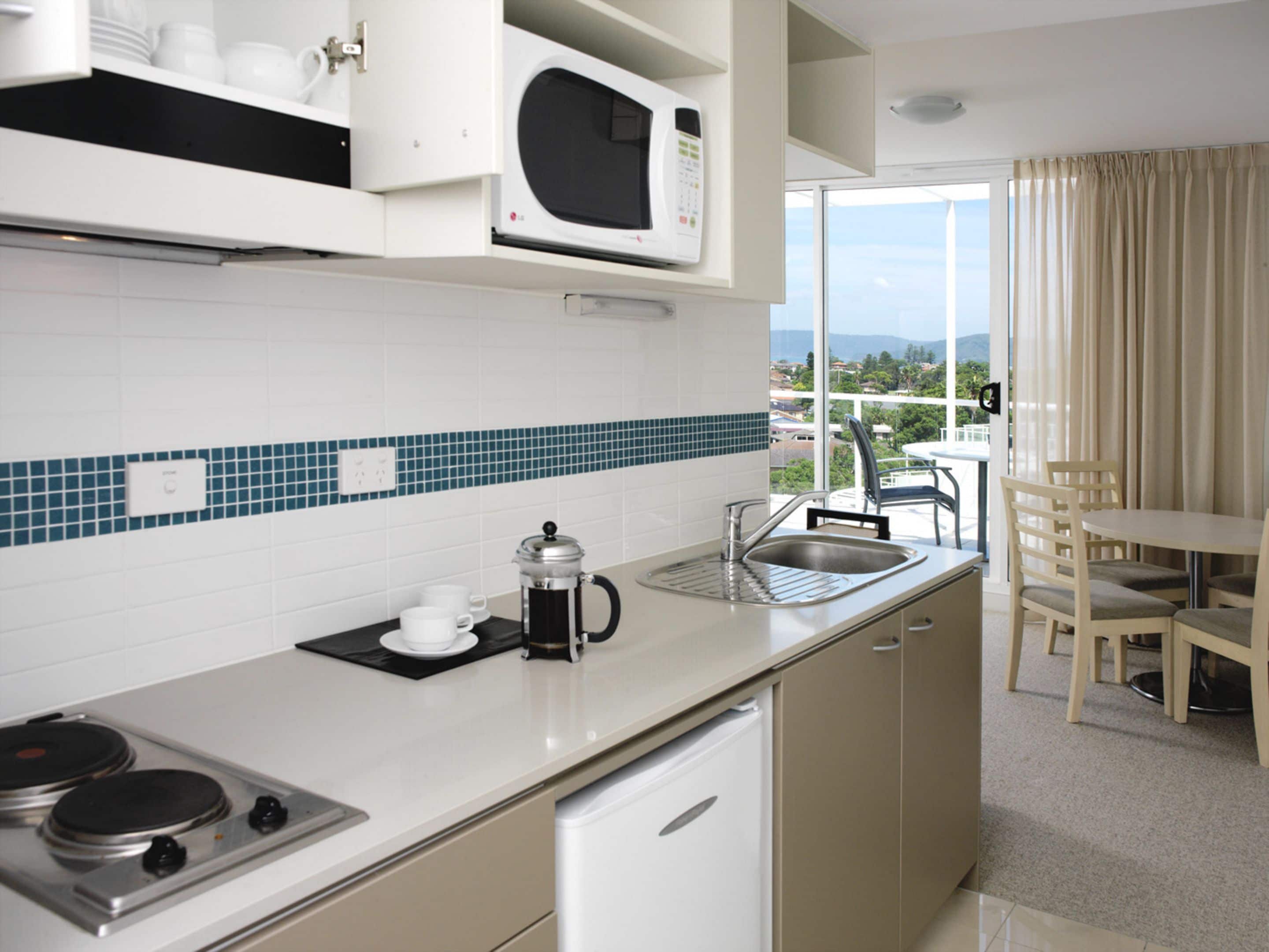 A modern kitchen with a microwave, coffee maker, and sink. There is a dining area with a table and chairs.