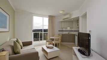 Una habitación de hotel moderna con sofá, una mesa de centro, televisor, zona de comedor con sillas y cocina equipada con microondas.