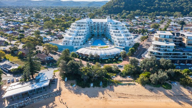 Un hotel grande con un patio central y varios balcones, rodeado por una zona residencial y una playa.