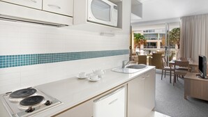 Una cocina moderna con armarios blancos, un microondas, una estufa y un lavaplatos. Se ve un área de comedor con una mesa y sillas a través de una puerta abierta.