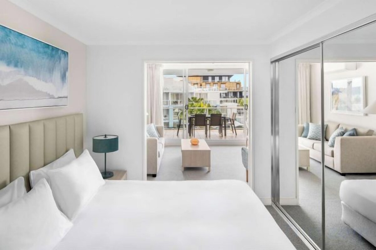 Habitación de hotel con cama, escritorio, silla y balcón con vistas a la ciudad.