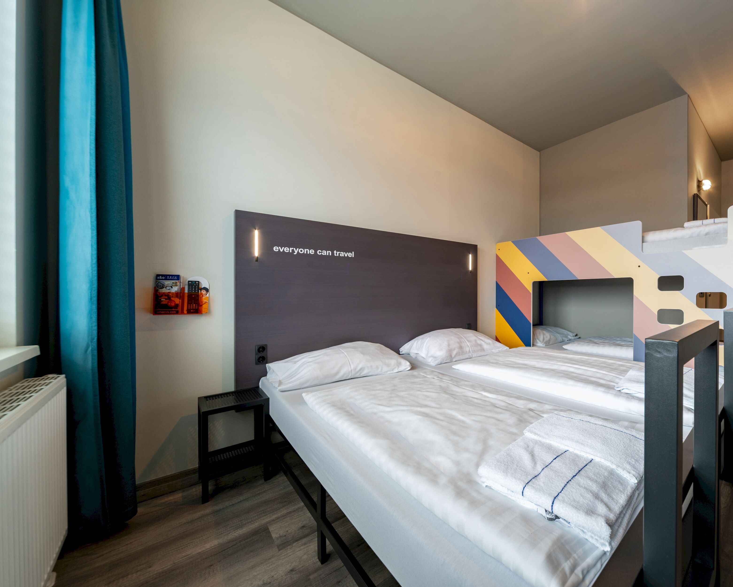 A modern hotel room with a large bed, a small bedside table, and a headboard with a motivational quote.
