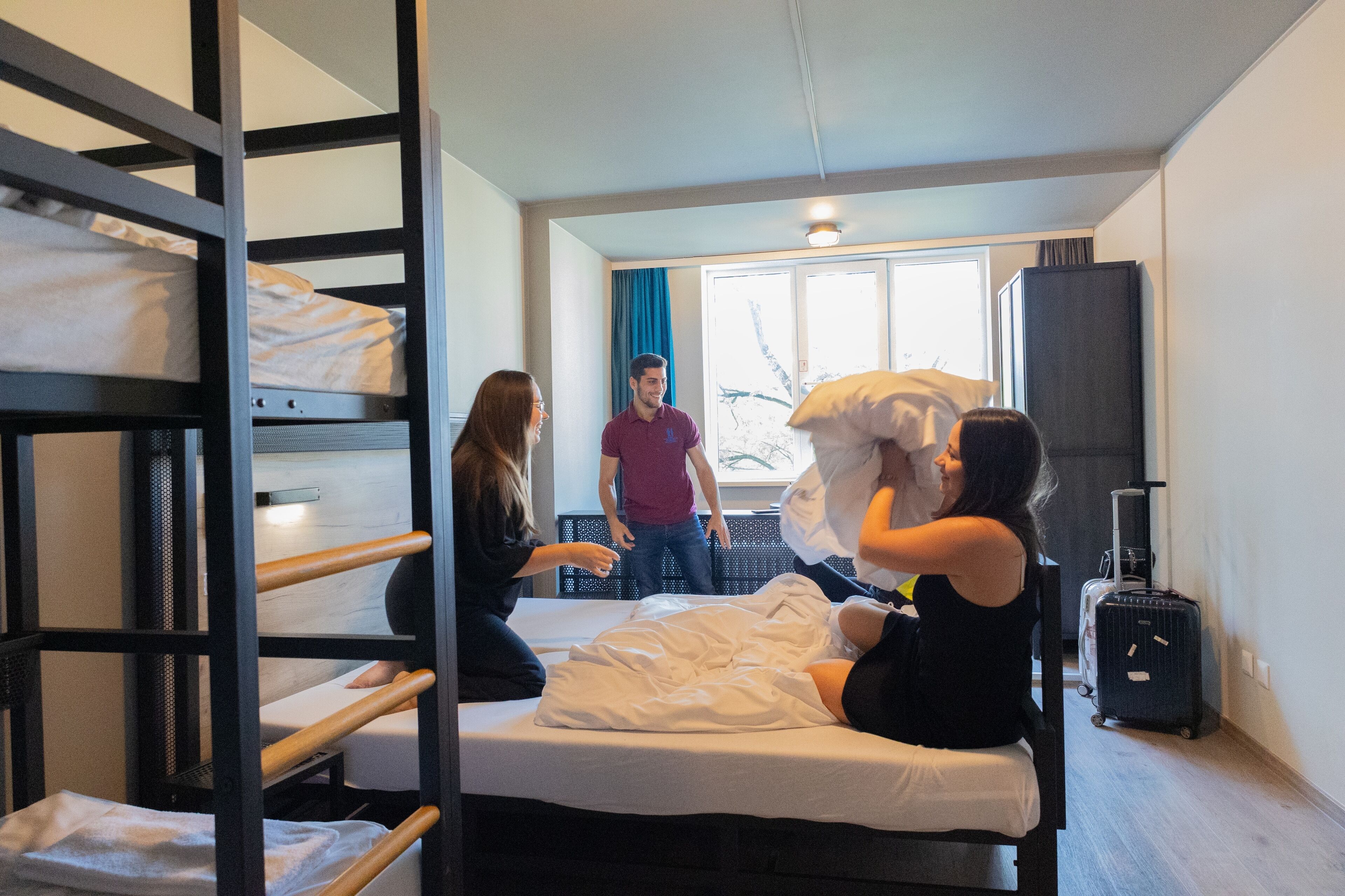 A bunk bed room with a window, a suitcase, and a bed with pillows.