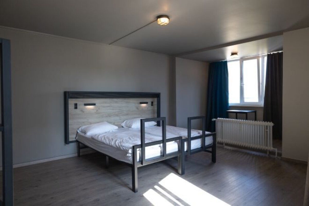 A bedroom with a bed, a radiator, and a window with curtains.
