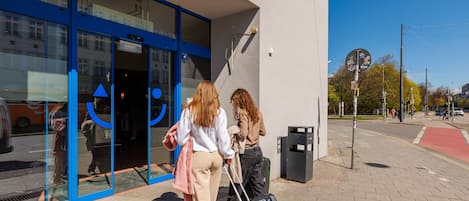 A building entrance with glass doors, a visible trash bin, and a clear sky.