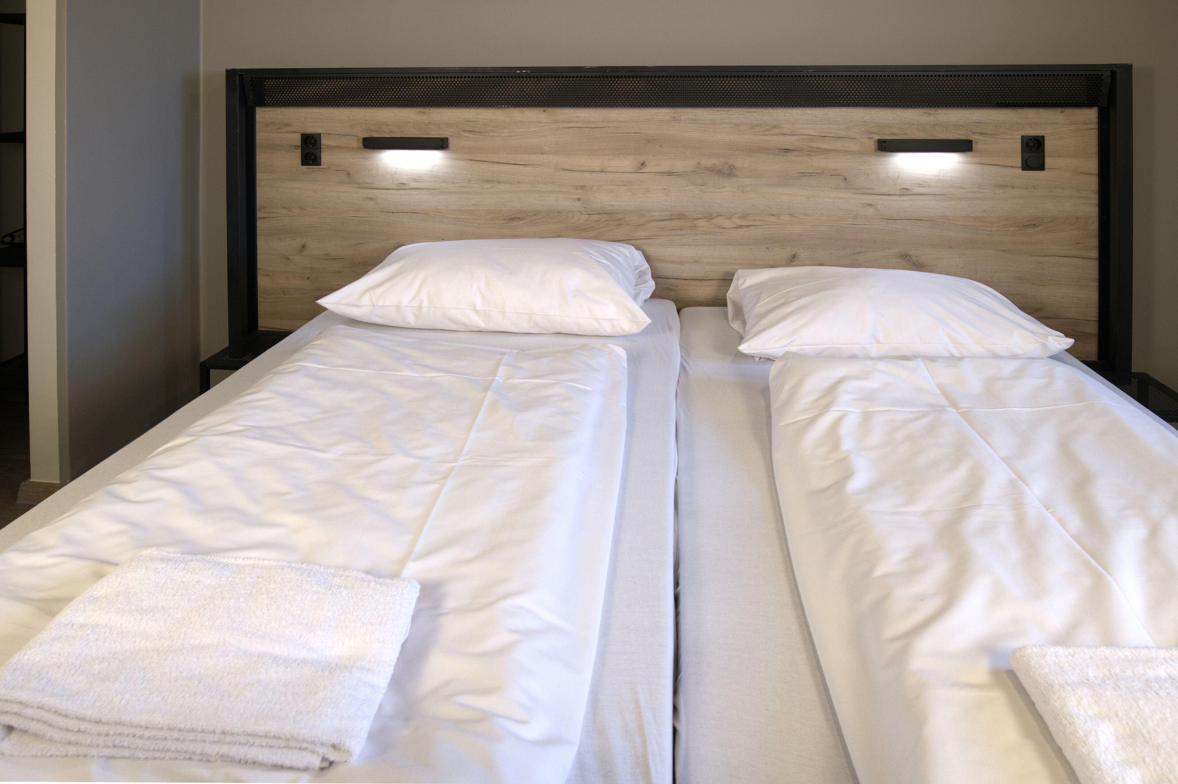 A double bed with white linens and pillows, a wooden headboard, and a small nightstand with a lamp.