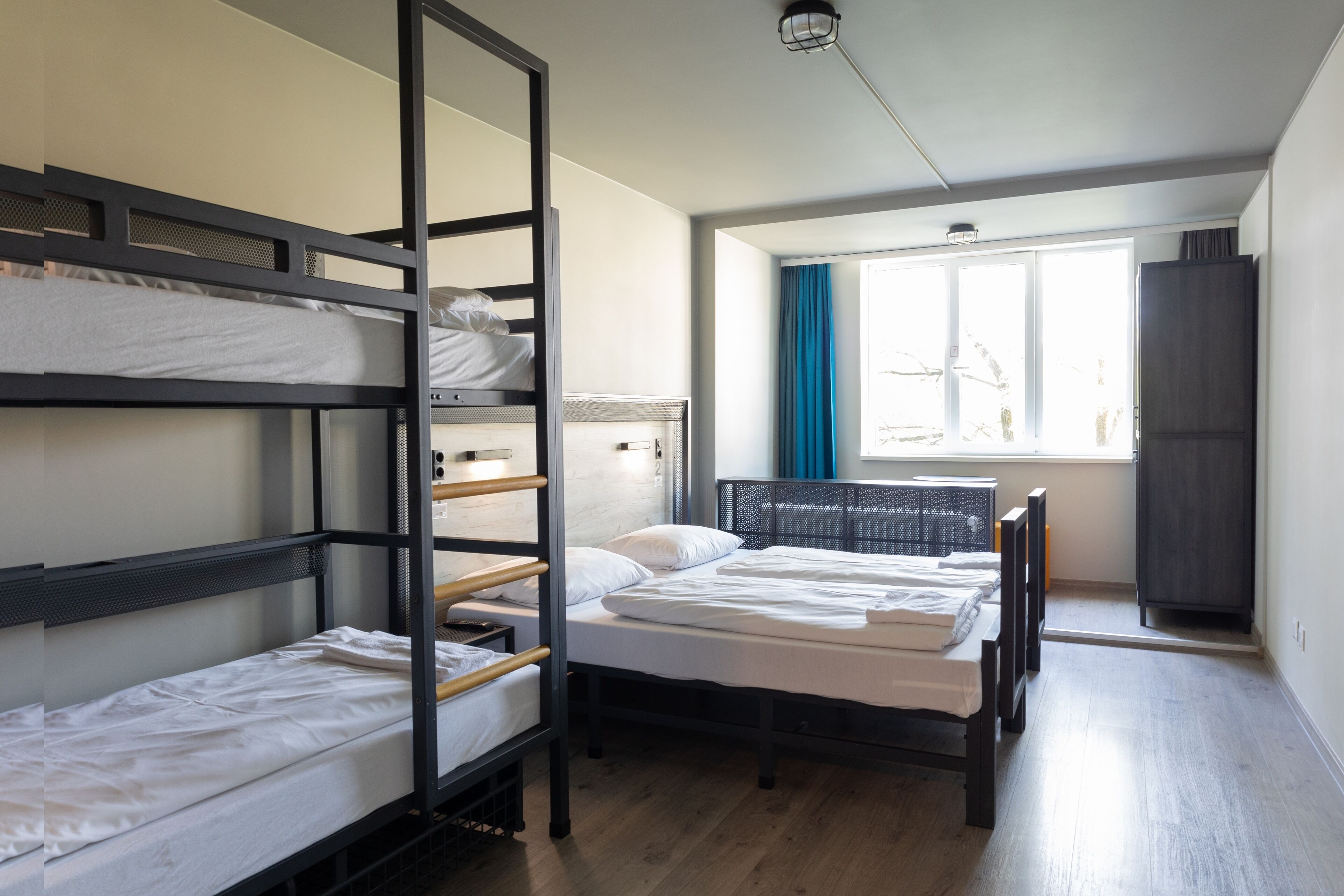 A dormitory-style room with bunk beds, a window with curtains, and a wardrobe.