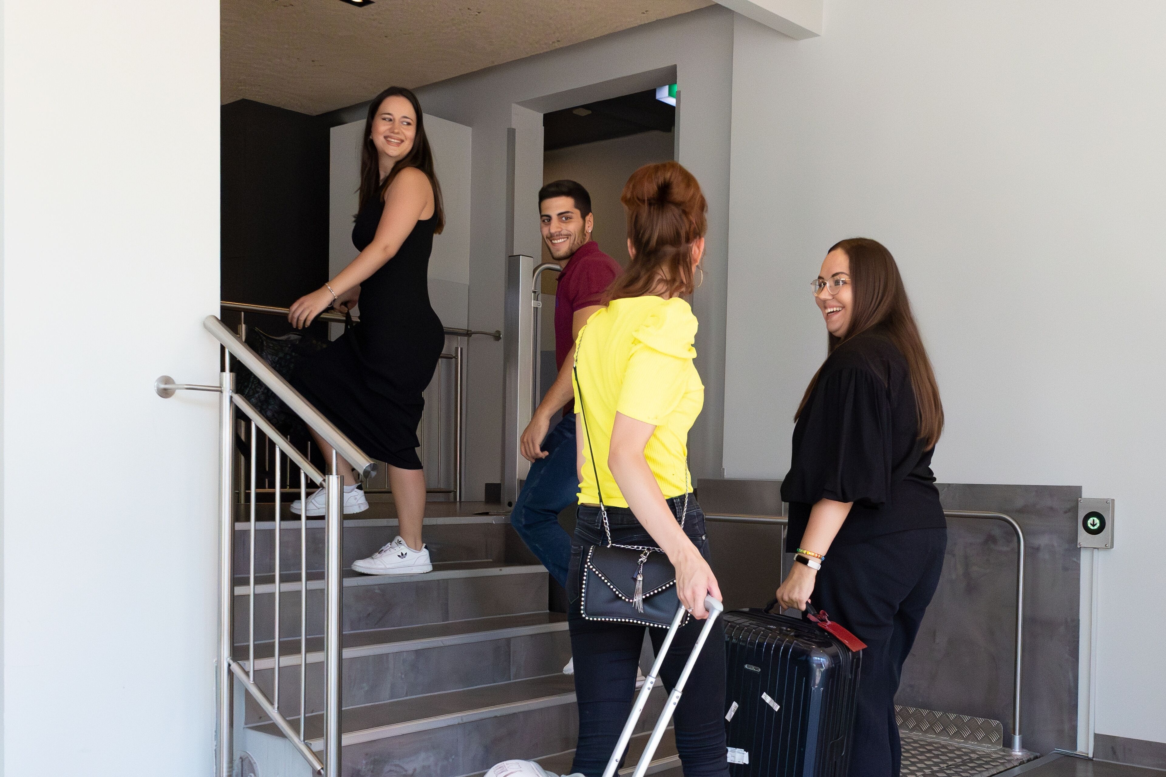 A group of people ascending a staircase in a modern building with metal railings and a glass elevator door.