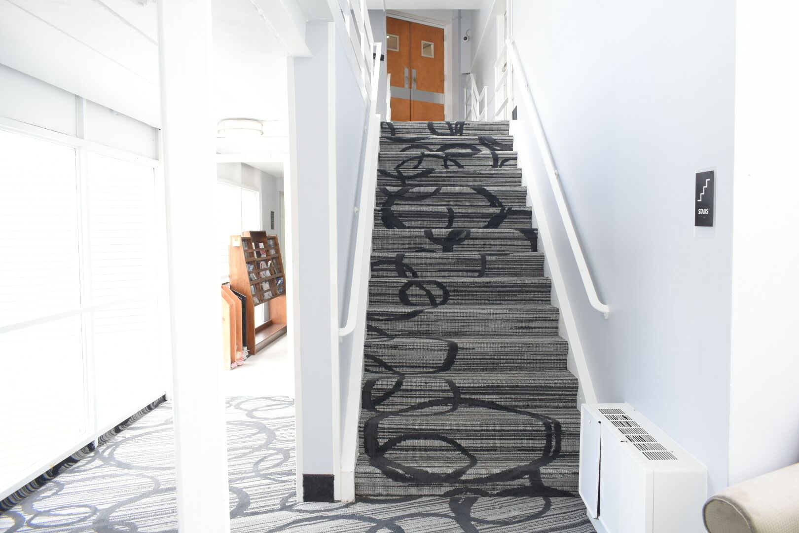 A staircase with a patterned carpet, white walls, and a door at the top.