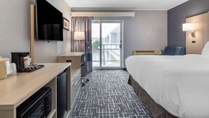 A hotel room with a bed, a desk with a flat-screen TV, a coffee maker, a microwave, a vacuum cleaner, and a sliding door to a balcony. - Comfort Inn Hyannis - Cape Cod (Hyannis)