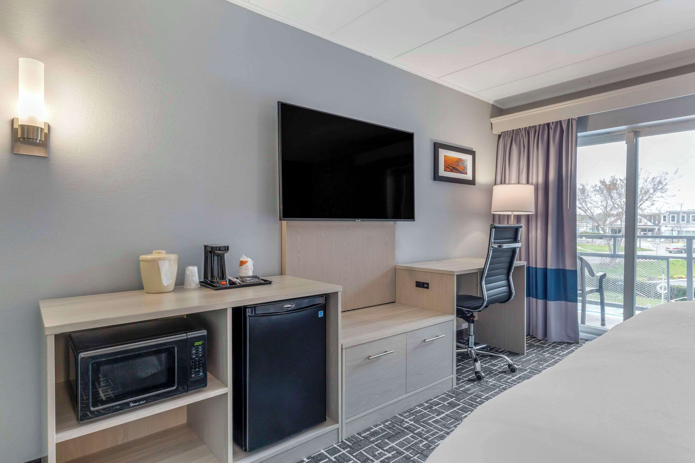 Habitación de hotel con televisión de pantalla plana, microondas, refrigerador pequeño, escritorio con silla y cama grande.