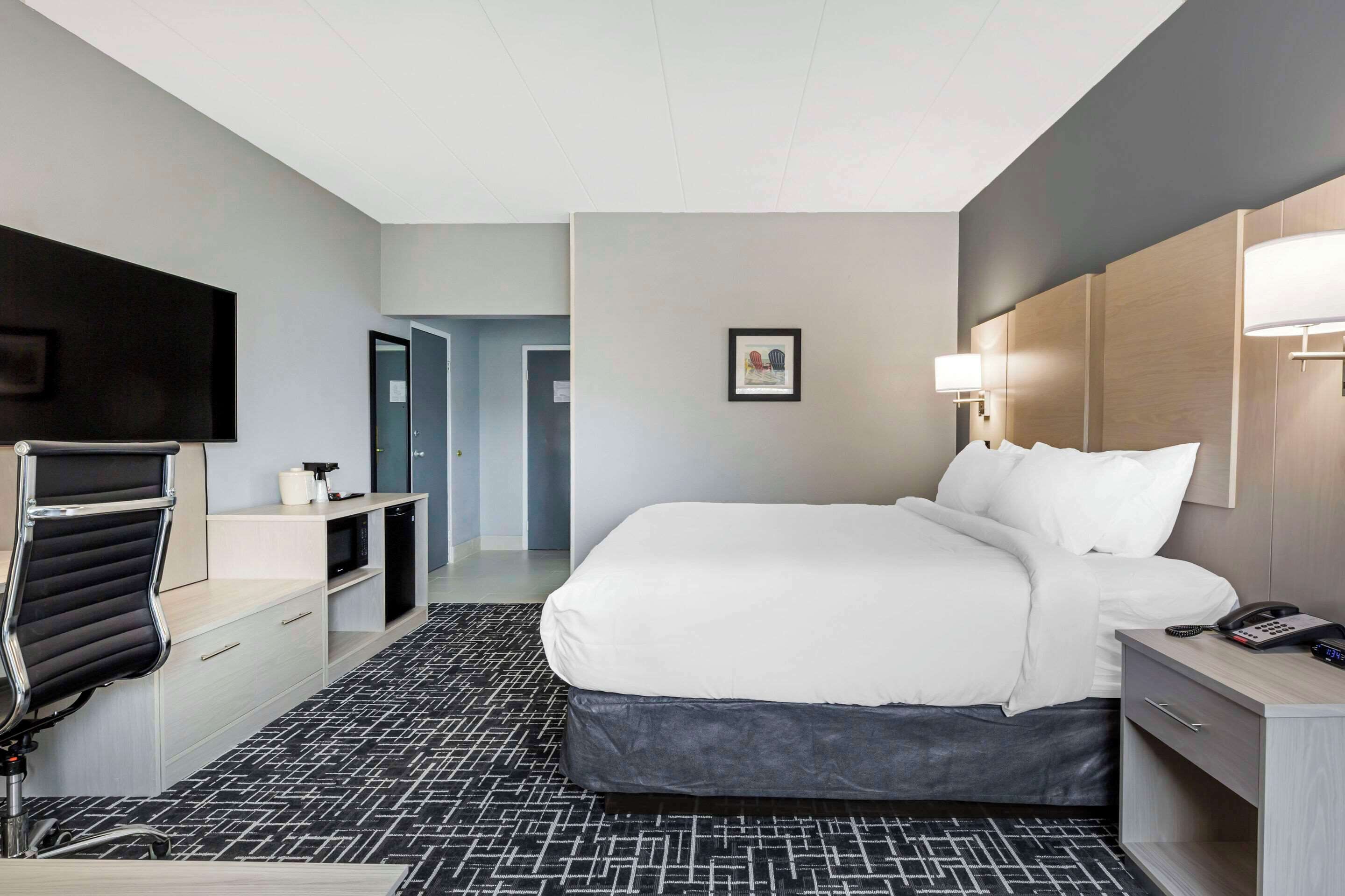 A hotel room with a large bed, a desk with a chair, a flat-screen TV, and a bedside lamp.