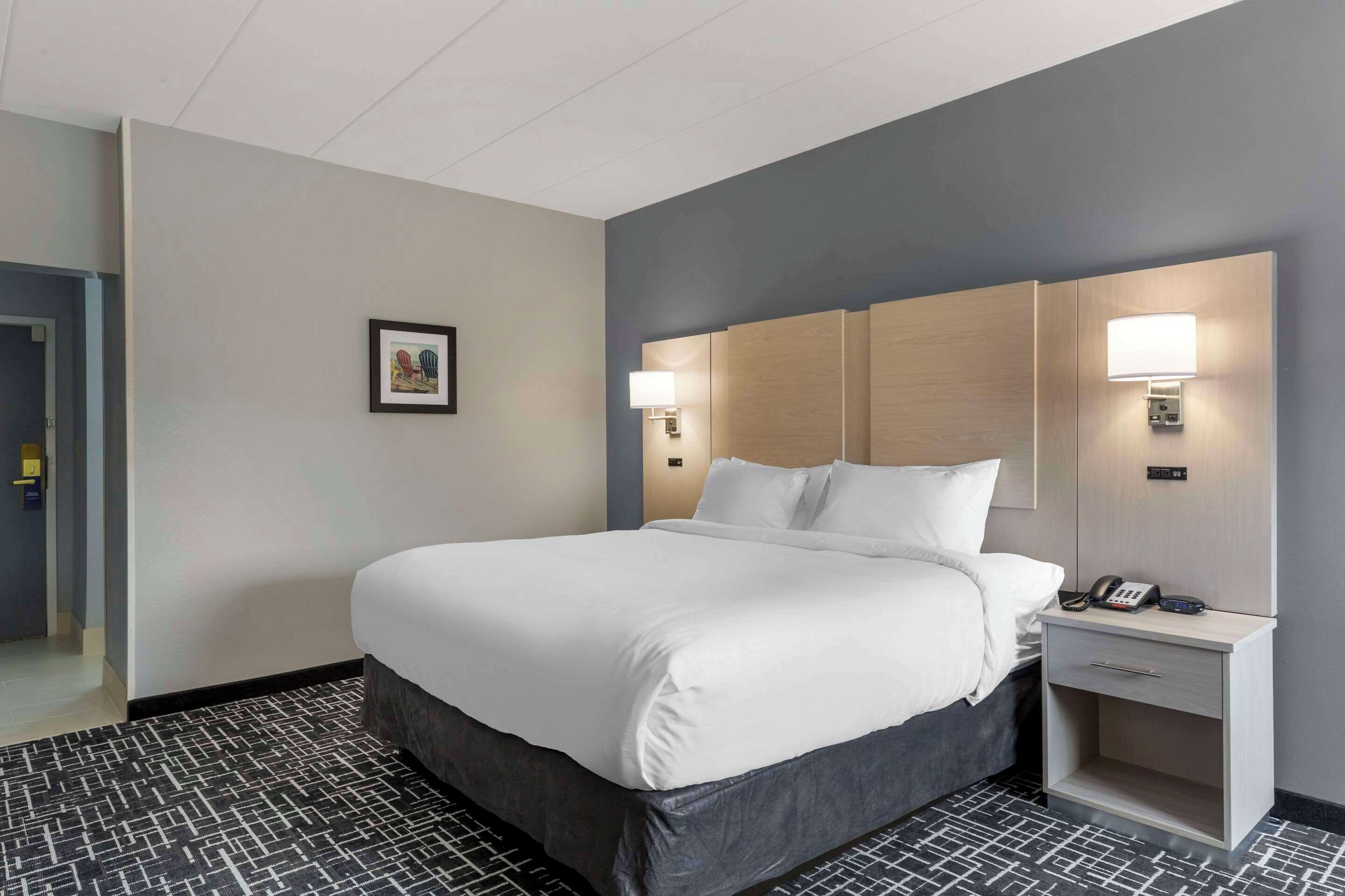 A hotel room with a large bed, bedside lamps, a nightstand with a phone, and a framed picture on the wall.