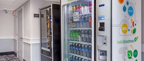A vending machine stocked with various beverages, a security camera, and a door with a sign.