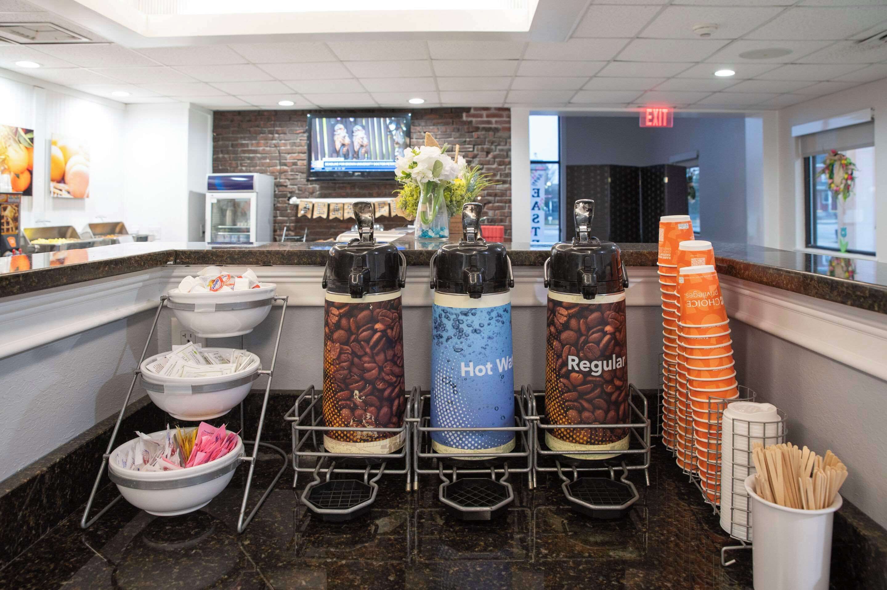 Un coin café équipé de distributeurs étiquetés « Eau chaude », « Café normal » et « Café », ainsi qu’un récipient contenant des ustensiles.