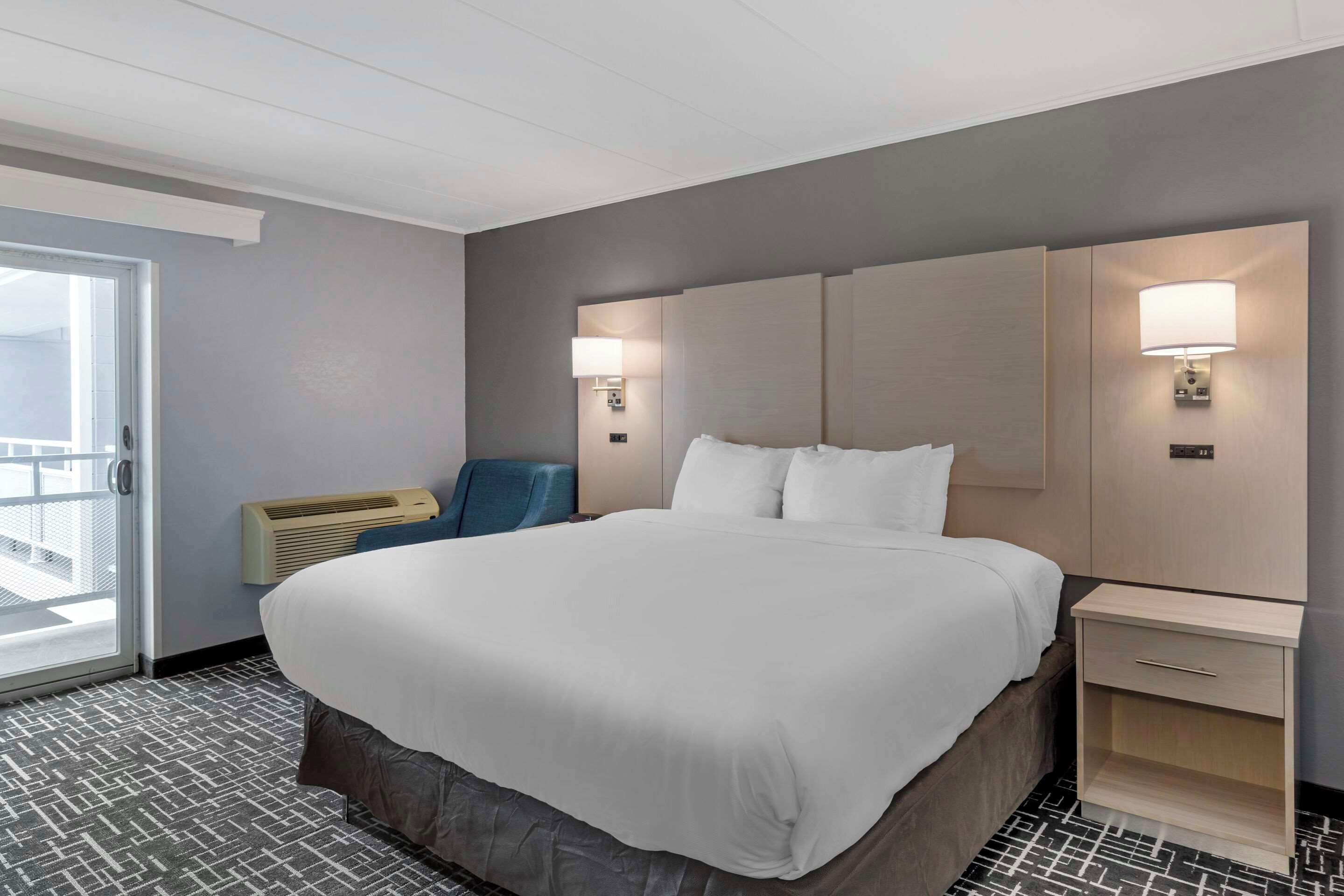 A hotel room with a large bed, two bedside tables, a chair, and a sliding glass door to the balcony.