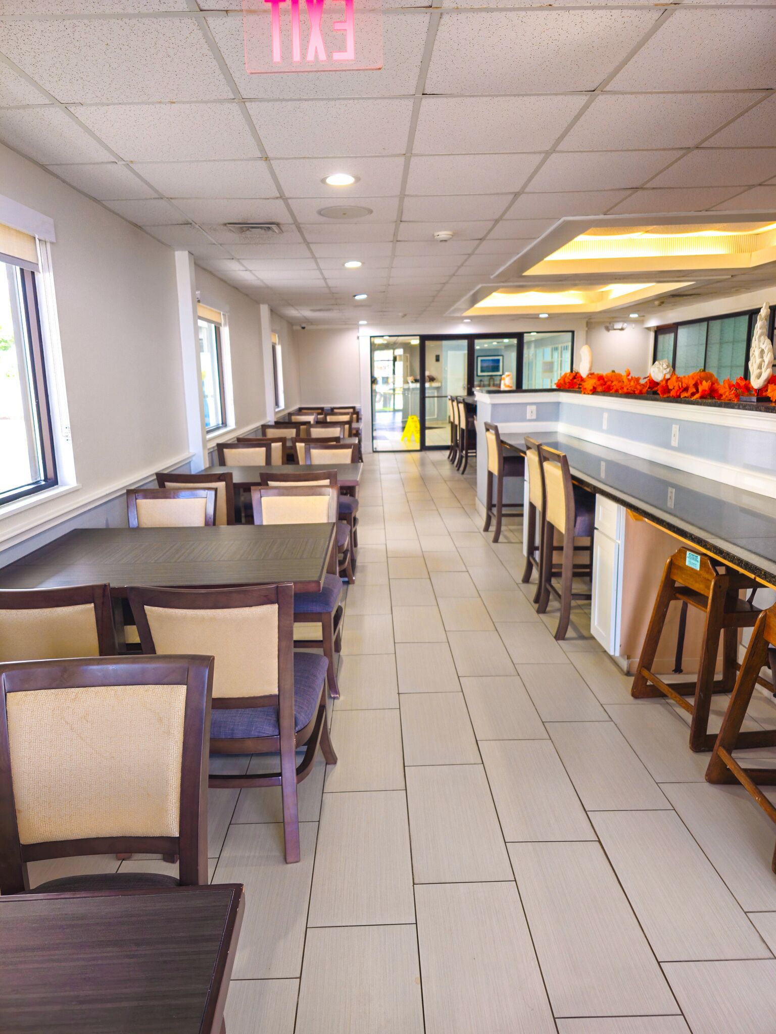 Una cafetería amplia con mesas y sillas largas, un mostrador con exhibición y un letrero de salida.