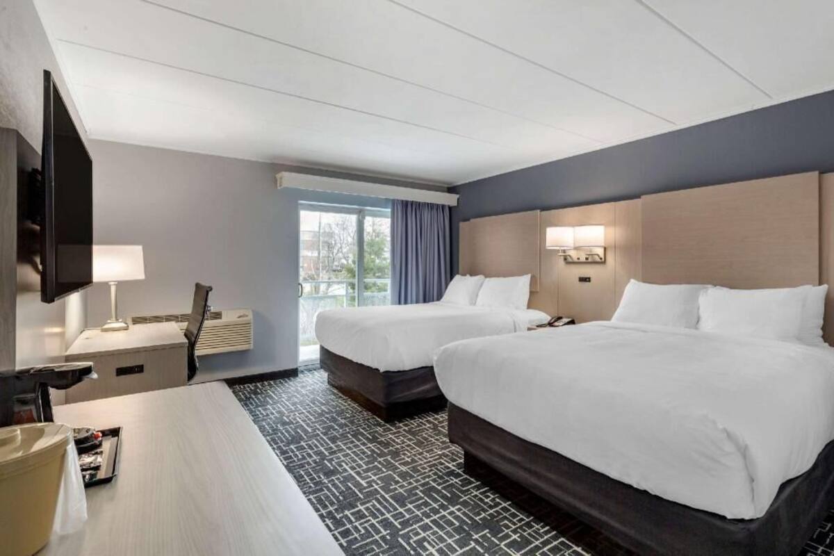 A hotel room with two beds, a desk with a chair, a TV, and a window with curtains.