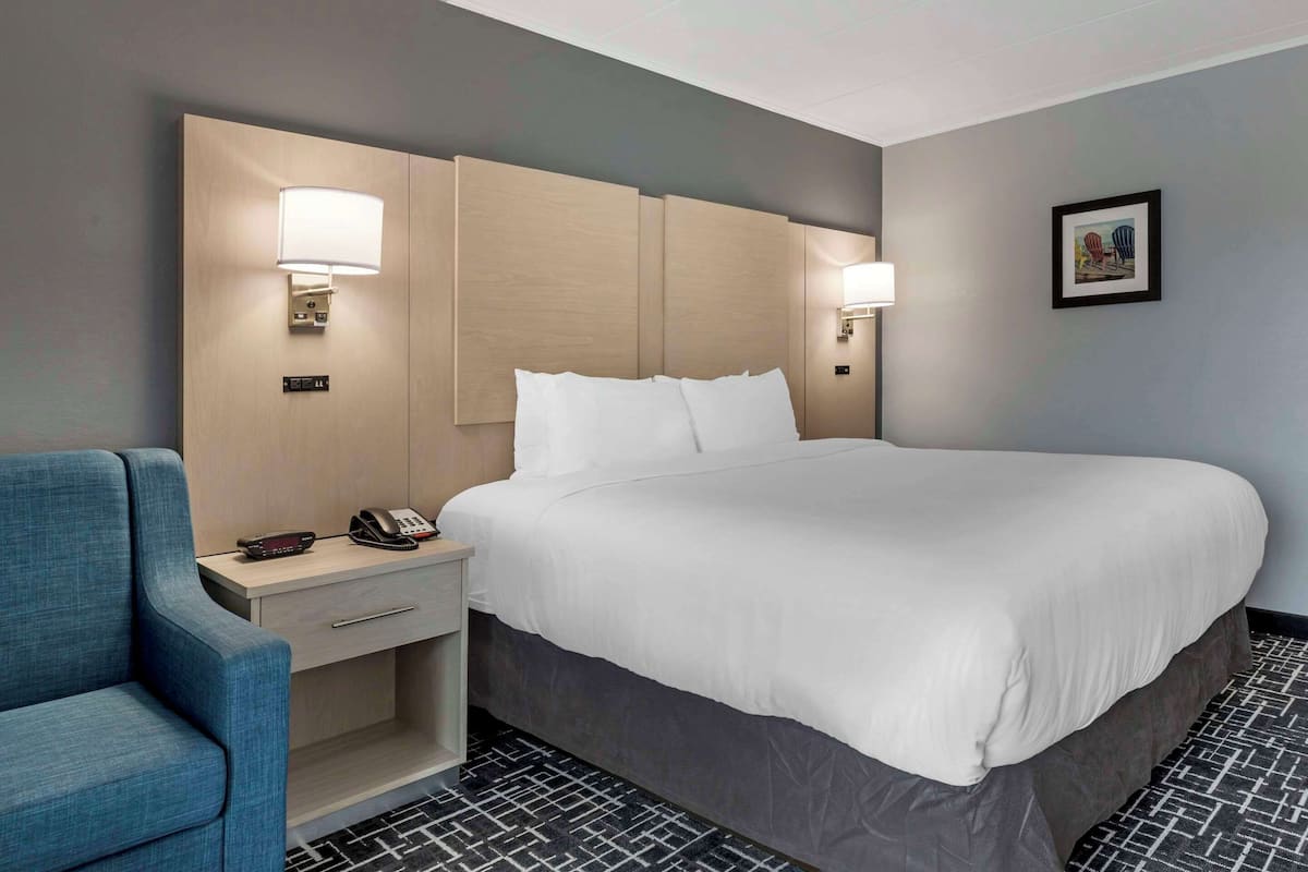A hotel room with a large bed, bedside lamps, a desk with a phone, and a blue chair.