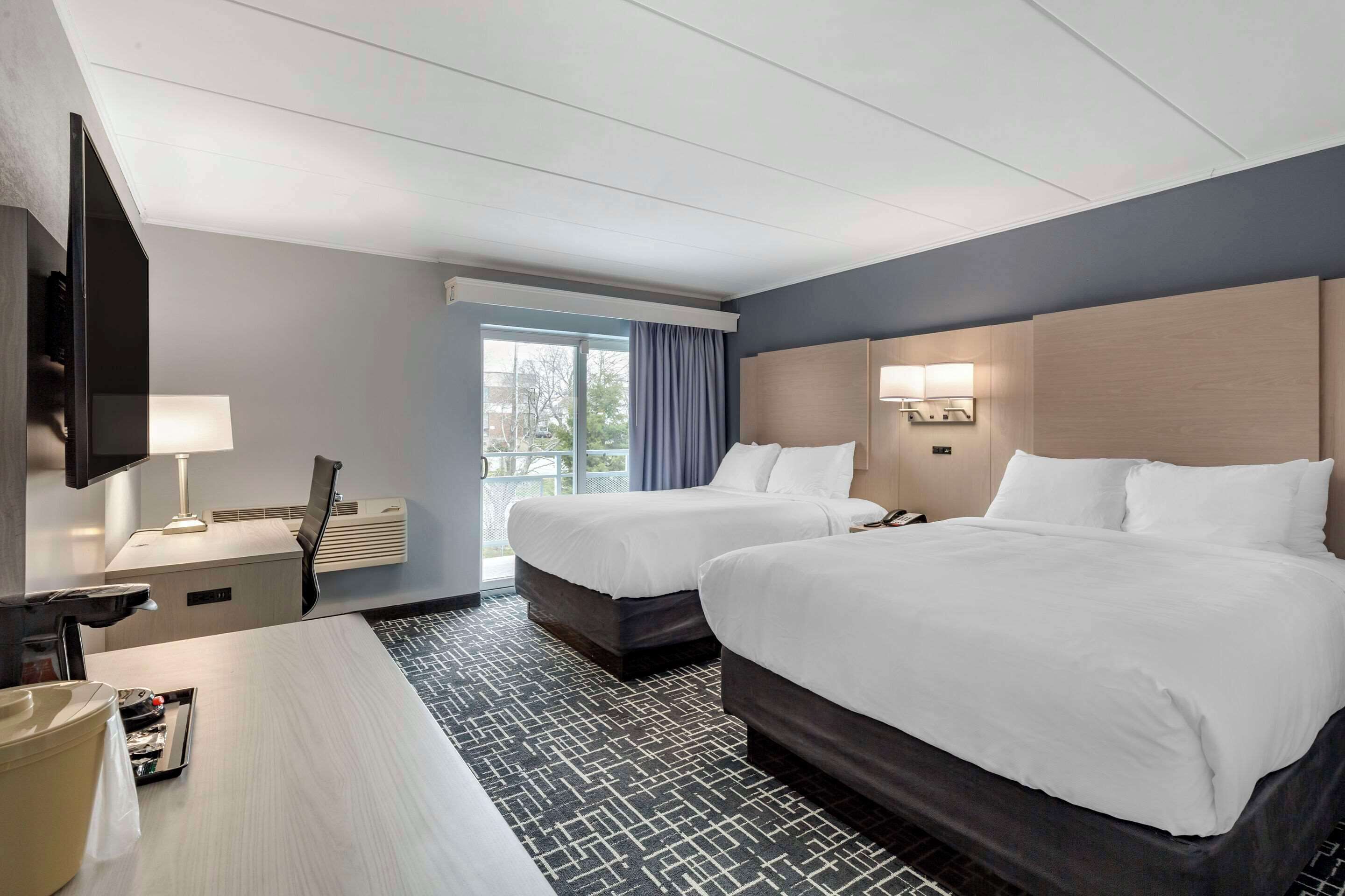 A hotel room with two beds, a desk with a lamp, a TV, and a window with curtains.