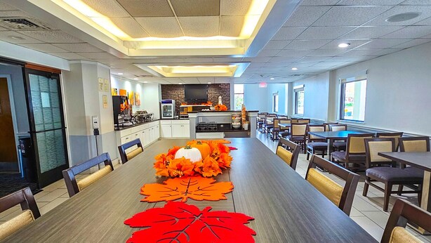 A long dining table with chairs, a kitchen area, and a large window. - Comfort Inn Hyannis - Cape Cod (Hyannis)
