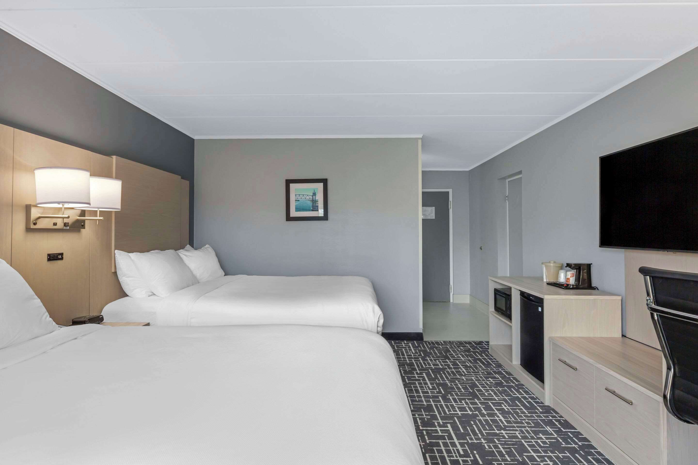 Quarto de hotel com duas camas, uma mesa de trabalho com televisão e uma pequena copa.