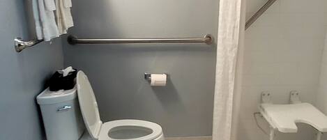 Un baño con inodoro, barra de apoyo, toallero y un pequeño banco.