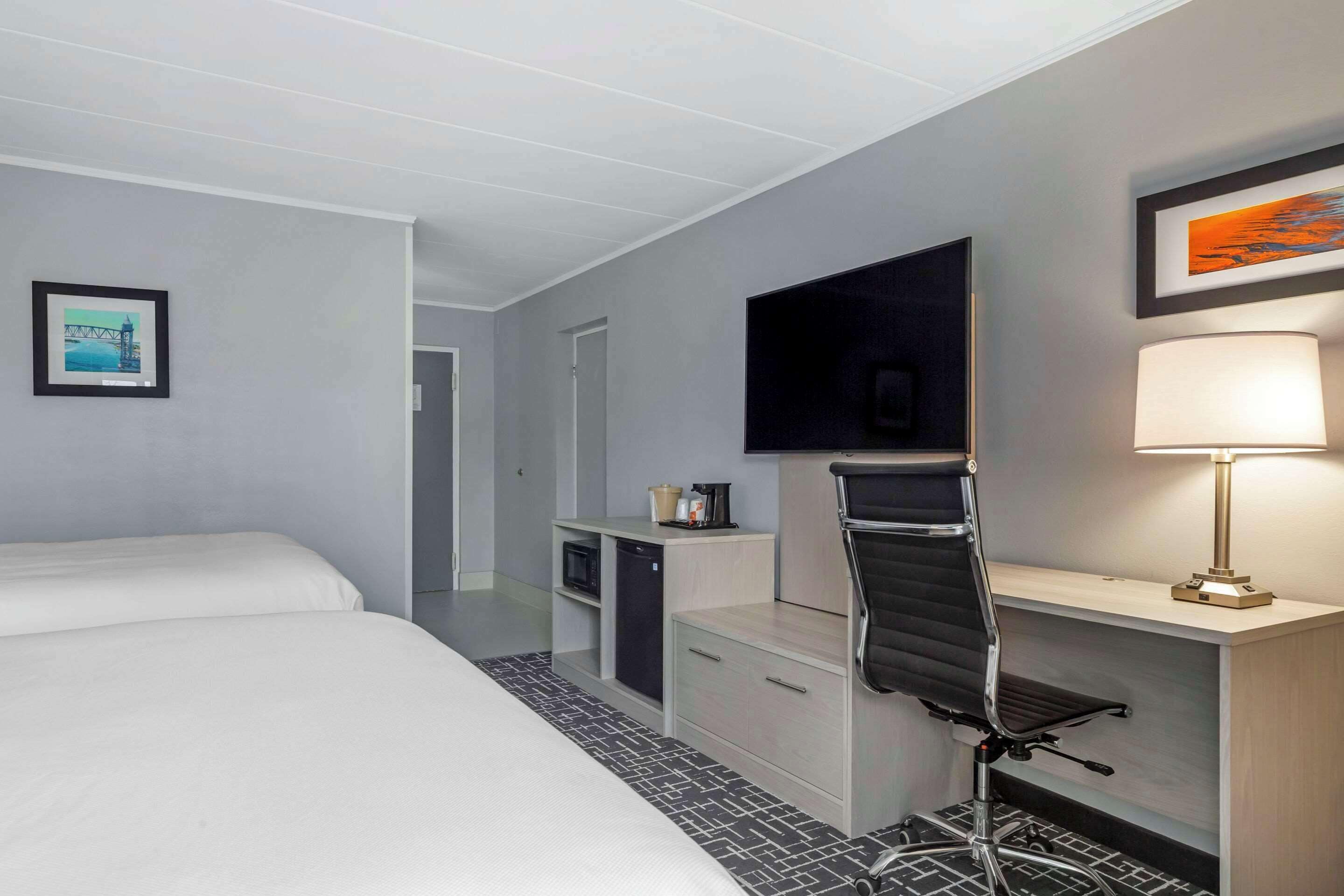 Ein Hotelzimmer mit Bett, Schreibtisch mit Stuhl, Fernseher, Lampe und einer kleinen Küchenzeile.