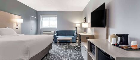 A hotel room with a large bed, a sofa, a desk with a coffee maker, and a TV mounted on the wall.