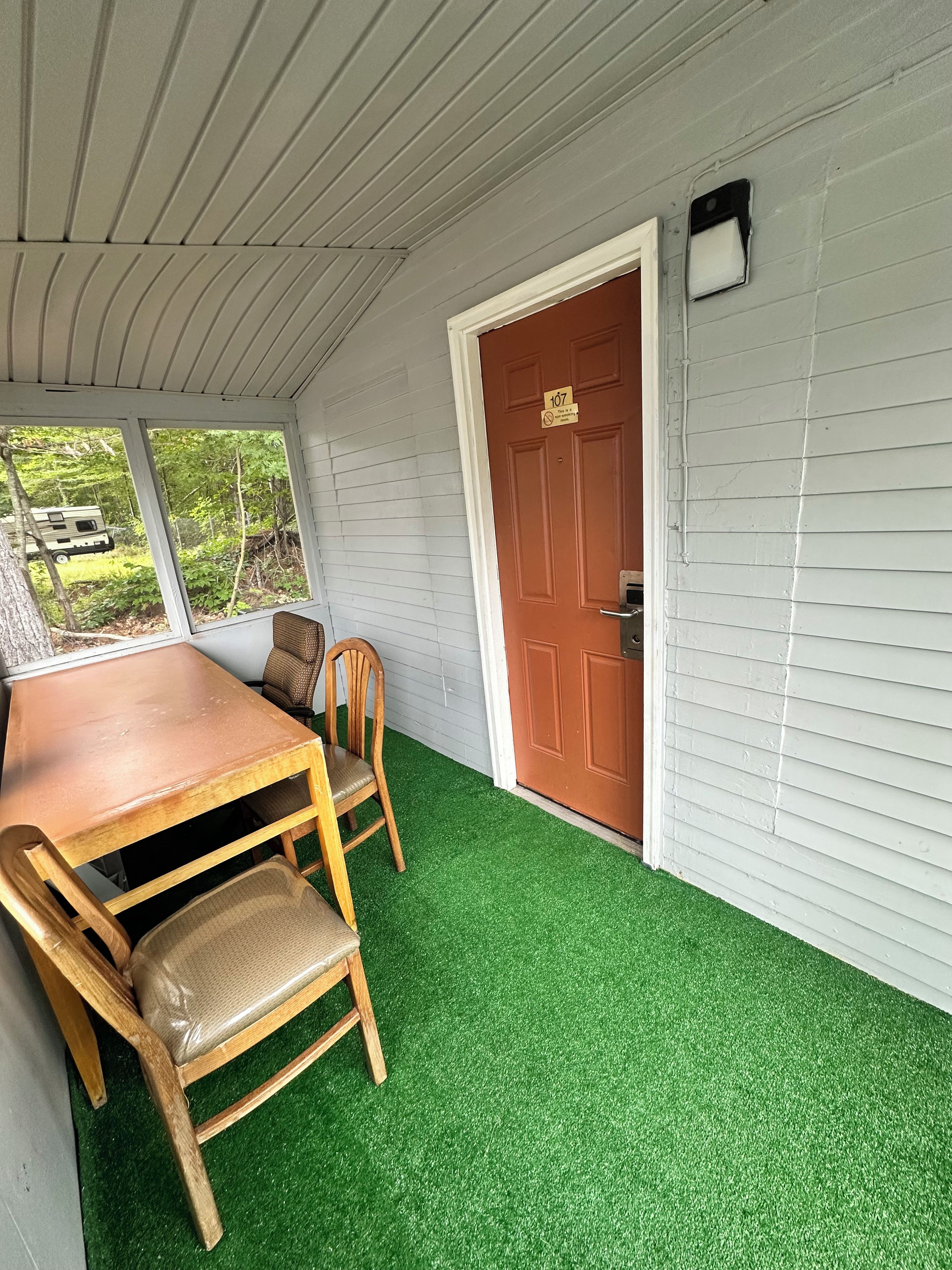 Une pièce avec une table et des chaises en bois, une porte marron et une fenêtre donnant sur un espace verdoyant.