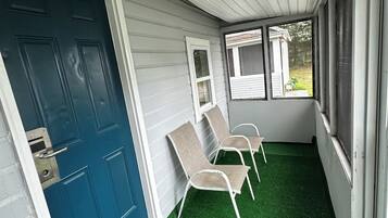 A covered porch with a blue door, two chairs, and a window.