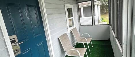 A covered porch with a blue door, two chairs, and a window.